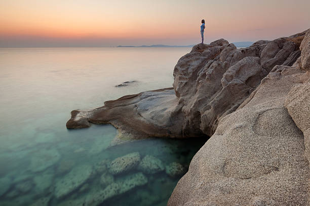 istock Solitude girl watching sunrise high up on cliff by sea 587817868