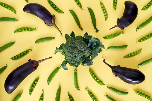 Pea pods and eggplants placed around broccoli