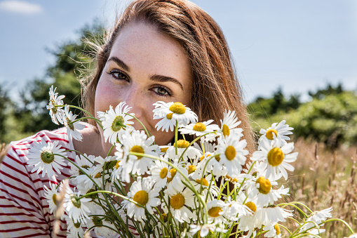 beautiful young woman with a field flower bouquet in the foreground smiling for natural beauty in summertime daylight