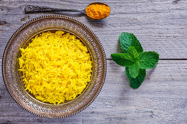 Antique Bowl with Turmeric Jasmine Rice Top view of an antique metal bowl with cooked turmeric jasmine rice, mint leaves and vintage teaspoon filled with powdered curcumin jasmine rice stock pictures, royalty-free photos & images
