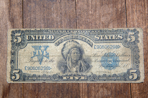 This is a photo of a very old bank note. It is a five dollar bill dated in 1899. It is very old and wrinkled and is shot on a wood background. This was how the US currency looked at that time and was issued from banks, not the US treasury.