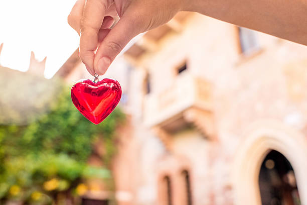 Holding a decoration in form of heart with Romeo and Juliet balcony on the background in Verona city