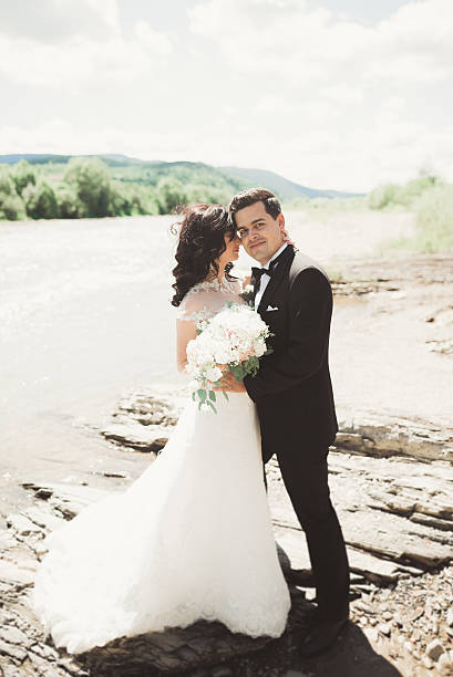istock Bride and groom holding beautiful wedding bouquet. Posing near river 587936290