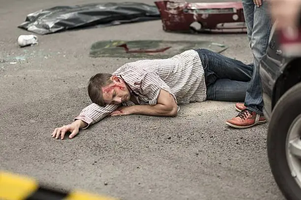 Man injured in car accident with blood on head lying on street.