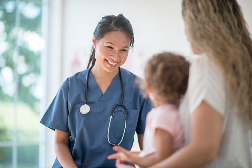 A little girl is at the doctors office for a check up. A nurse is sitting with them and talking to the mother.