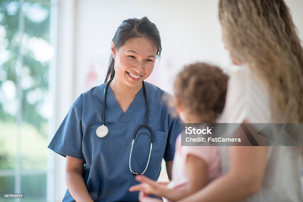 Nurse Speaking to a Mother and Child A little girl is at the doctors office for a check up. A nurse is sitting with them and talking to the mother. Nurse Stock Photo