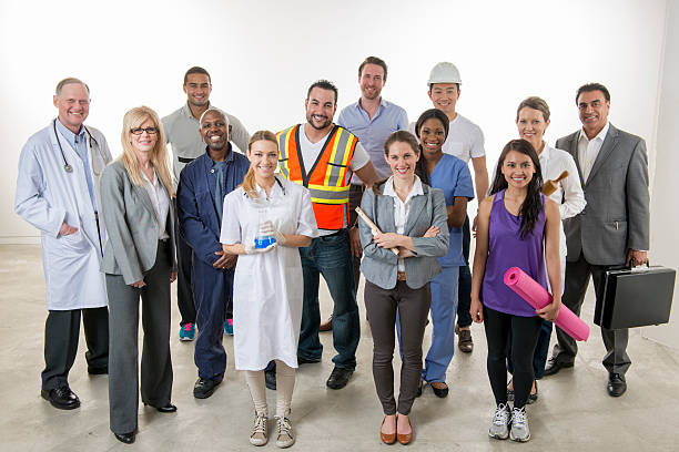 Professionals Standing Together A multi-ethnic group of professional adults are standing together in a group. There is a nurse, yoga teacher, scientist, chemist, doctor, teacher, construction worker, mechanic, and business professionals. various occupations stock pictures, royalty-free photos & images
