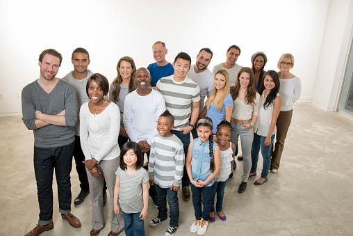 A multi-ethnic group of multi-generations are standing together in a group and are smiling while looking at the camera.