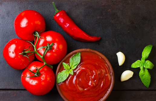 Tomato sauce salsa and ingredients - tomatoes, garlic, chili on dark stone background. Top view