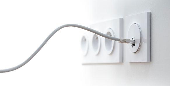 Close-up of an ethernet cable plugged into a wall socket, horizontal image with free space for text