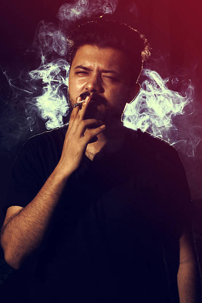 istock Young man smoking cigarette on dark background looking into camera 588226090