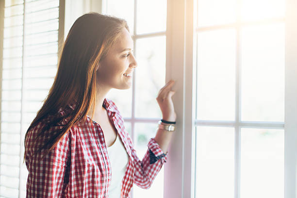 istock Smiling young woman looking through window 588243476