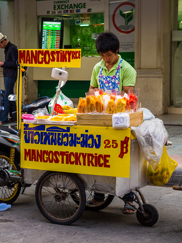 Bangkok, Thailand - June 18, 2012: A vendor stands by his food card selling mangoes and sticky rice in a street in Bangkok, Thailand.