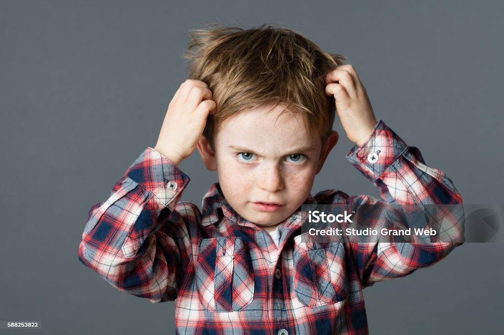 unhappy kid scratching his hair for head lice or allergies mischievous unhappy 6-year old kid with freckles scratching his hair for head lice or allergies, grey background studio Louse Stock Photo