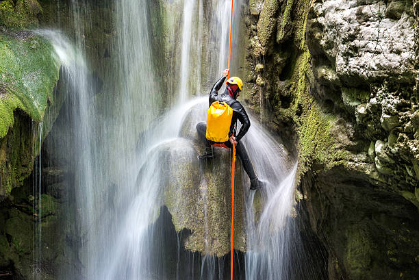 Canyoning adventure Canyoneering member with backpack rappeling down the waterfall in the canyon. canyoneering stock pictures, royalty-free photos & images