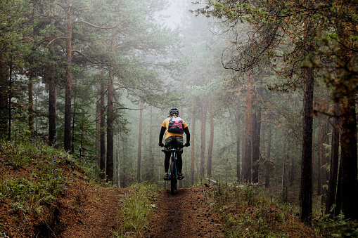 Revda, Russia - July 31, 2016: man mountainbiker rides on a sports  bicycle on a forest trail. in forest mist, mysterious view during Regional competitions on cross-country bike