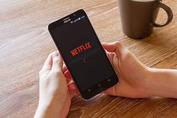 man hand holding screen shot of Netflix application Chiang Mai, Thailand - April 26, 2016: man hand holding screen shot of Netflix application showing on Asus Zenfone 2 mobile phone. Netflix is a global provider of streaming movies and TV series. editorial stock pictures, royalty-free photos & images