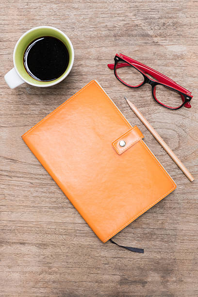 istock Orange leather diary pencil glasses and a cup of coffee. 588360214