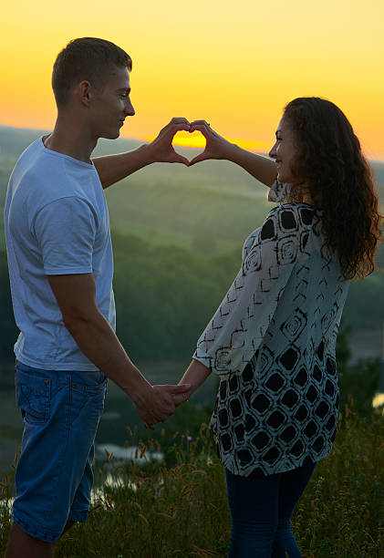 istock romantic couple at sunset make a heart shape from hands 588362588