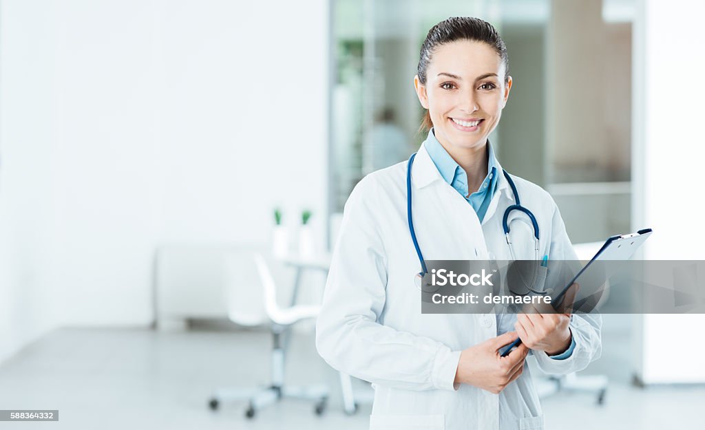 Smiling female doctor holding medical records Smiling female doctor with lab coat in her office holding a clipboard with medical records, she is looking at camera Doctor Stock Photo