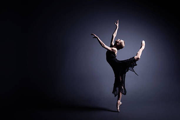 istock Young ballerina in a black suit is dancing in dark 588365934