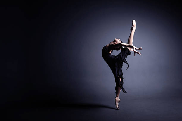 Young ballerina in a black suit is dancing in dark Young ballerina in a black suit is dancing in a dark studio ballet stock pictures, royalty-free photos & images