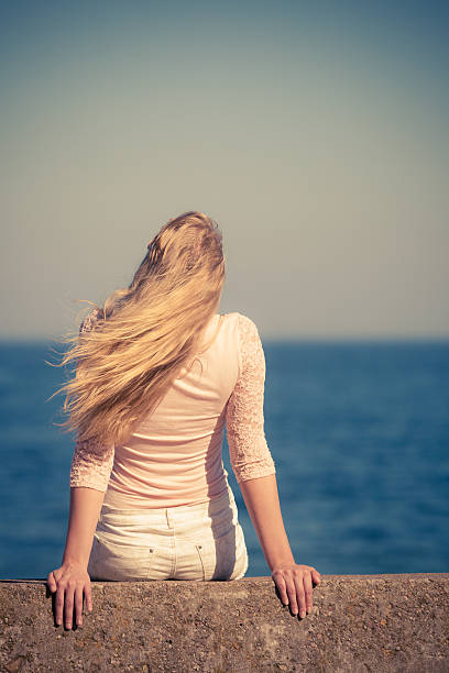 Vacation relax by seaside. Female look to sea horizon, enjoy her freedom and fresh air. Back view.