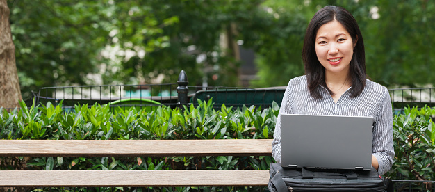 joven empresaria asiática sentada en el banco del parque trabajando en una computadora portátil photo
