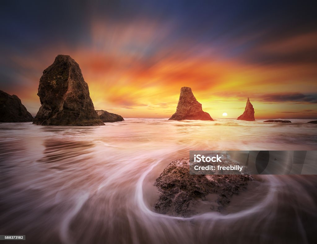 Three sisters with one sun This is a seascape photo with stacks, ocean flux, setting sun and colorful clouds. Bandon Stock Photo