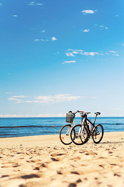 Pair of bikes left at the seaside on blue cloudy sky background. Multicolored vibrant summertime vertical outdoor image.