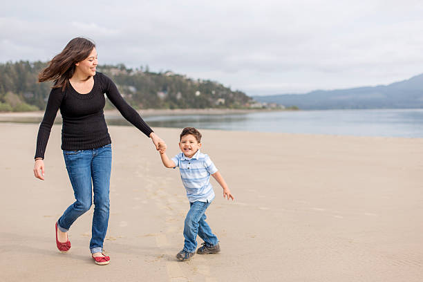 istock Young mom holding hands with her son at the beach 588374024