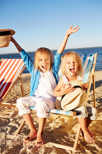 Two ecstatic little sisters sitting in deck chair on the beach