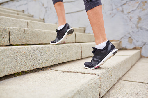 Feet of woman wearing sports shoes and walking up stairs on tiptoes
