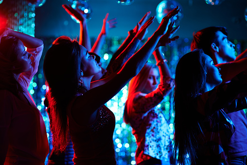 Social gathering of friends at party. Teenagers spending time in the nightclub. Spectators enjoying music concert. Young people waving their arms. It is perfect for using it in commercial and advertising photography, reports, books, presentation