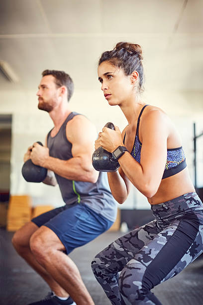 молодая женщина с инструктором подъема гири в тренажерном зале - gym muscular build weights two people стоковые фото и изображения