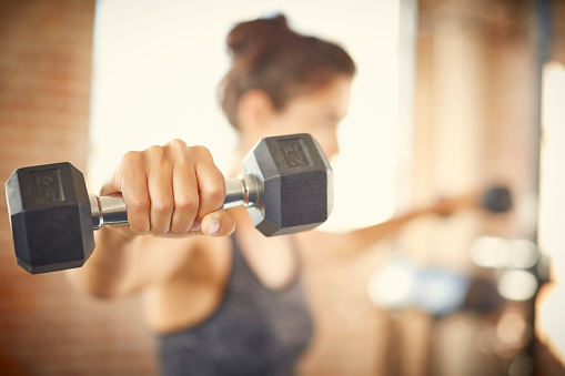 Close-up of dumbbell held by young woman. Fit female is exercising in gym. She is lifting weights.