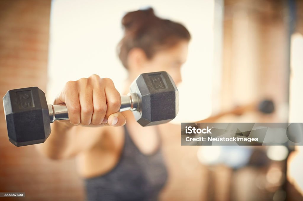 Close-up of dumbbell held by young woman in gym Close-up of dumbbell held by young woman. Fit female is exercising in gym. She is lifting weights. Dumbbell Stock Photo