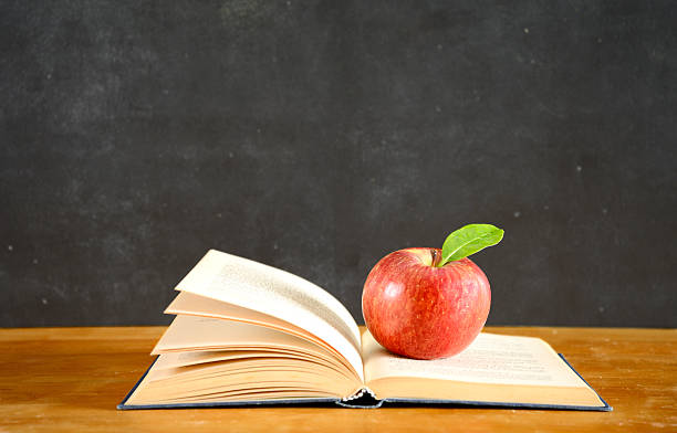 istock Apple on old book in front of blackboard. Copy Space. 588391942