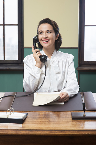 Smiling vintage receptionist working at office desk and smiling