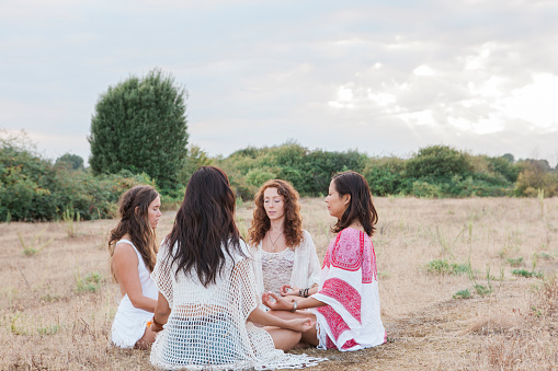 Boho women meditating in circle in rural field