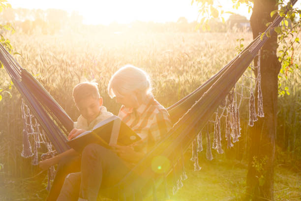 babcia i wnuk czytający książkę w słonecznym wiejskim hamaku - grandmother reading child grandson zdjęcia i obrazy z banku zdjęć