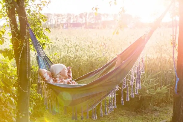 Photo of Serene woman napping in hammock next to sunny rural wheat field