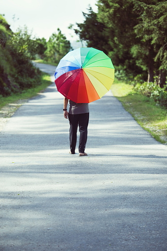 Rear view of a man standing with multi-colored umbrella in the middle of road