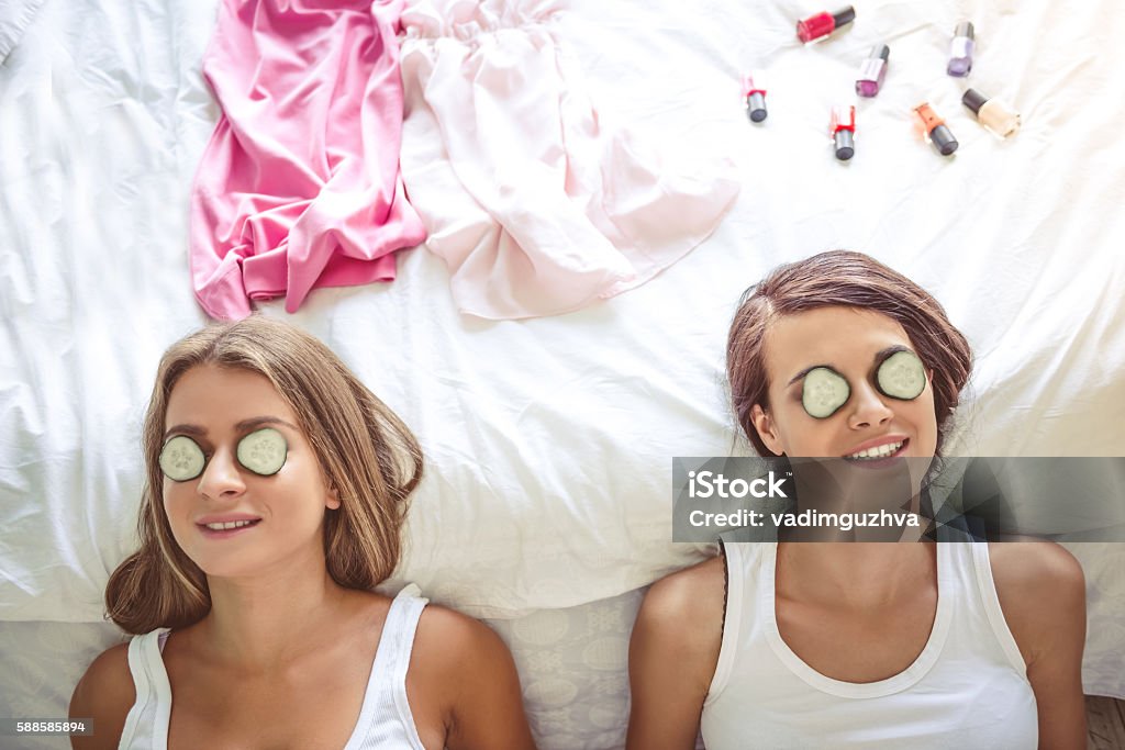 Girls at home Top view of two beautiful girls smiling while lying with cucumbers in their eyes on bed at home Bachelor Stock Photo