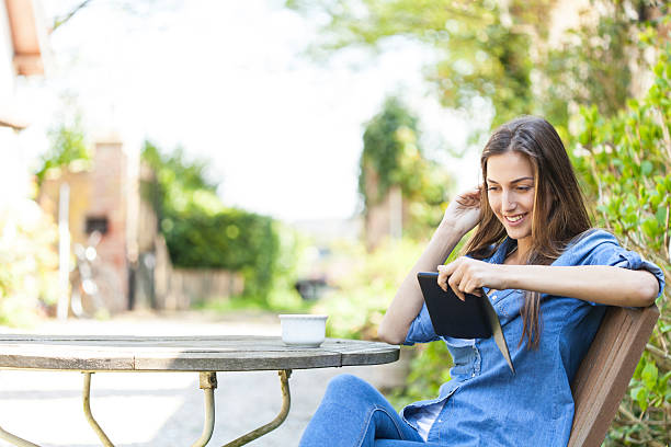Young woman sitting outdoors and reading a e-book