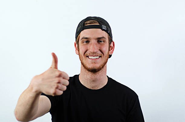 Smiling Young Adult Male Shows His Thumbs Up Smiling Young Adult Male in Dark T-Shirt and Baseball Hat Worn Backwards Shows His Thumbs Up back to front stock pictures, royalty-free photos & images