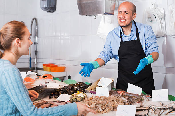 istock Smiling seller helping female customer to choose  fish 588592340