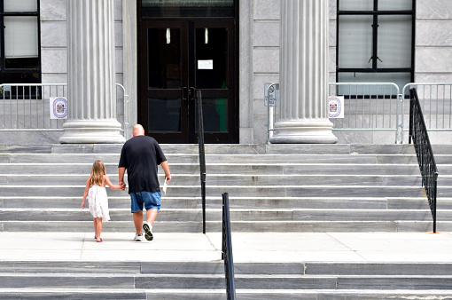 Norristown, PA., USA - August 8, 2016; A child holds the hand of a man as they walk up the steps towards the main entrance of Montgomery County Court House, in Norristown, Pennsylvania.