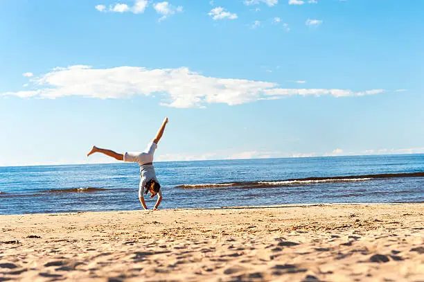 Photo of Cheerful teenage girl doing handstand on the beach sand