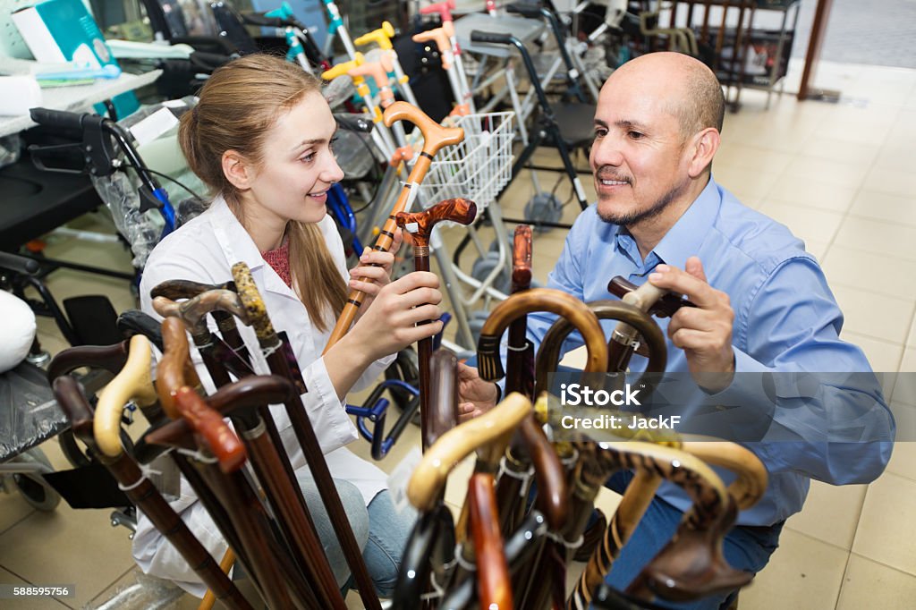 Physician offering cane to customer Female physician offering a lightweight cane to customer in a orthopaedic store. Focus on both persons Walking Cane Stock Photo